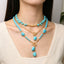 Model wearing layered turquoise-colored beads and gold-tone chains with drop pendants