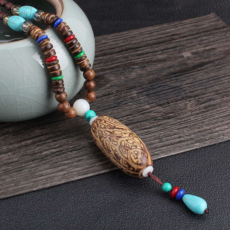 Close-up of a patterned oval necklace pendant with turquoise-colored accent beads
