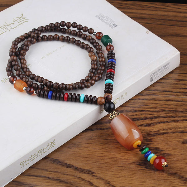 Brown beaded necklace with amber-colored oval pendant and multicolor accents on a white book