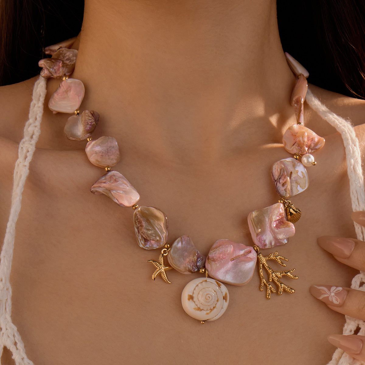 Pink shell-style necklace with gold-tone coral and starfish charms, worn by a model