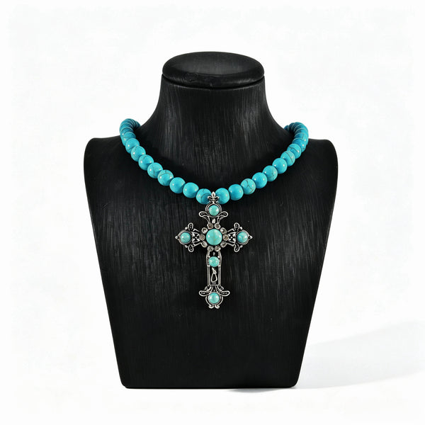 Turquoise-colored beaded necklace with ornate cross pendant on a black display bust
