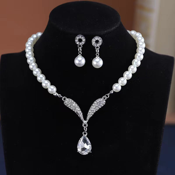 White pearl-style necklace and teardrop earrings displayed against black