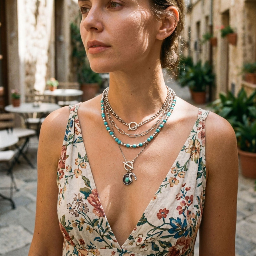 Layered turquoise-colored beaded necklaces with small silver-tone pendants over a floral dress