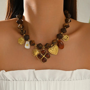 Brown beaded necklace with gold-tone heart, flower and leaf charms, worn by a model