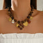 Brown beaded necklace with gold-tone heart, flower and leaf charms, worn by a model