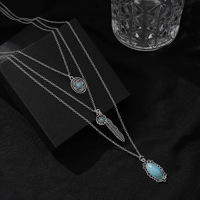 Layered silver-tone pendant necklaces with turquoise-colored accents on a black display