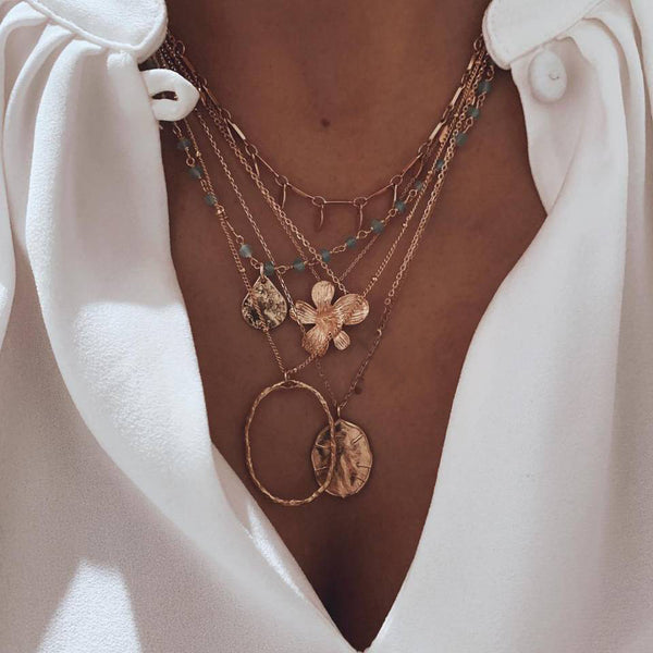 Layered gold-tone necklaces with flower, leaf and circular pendants, worn with a white shirt