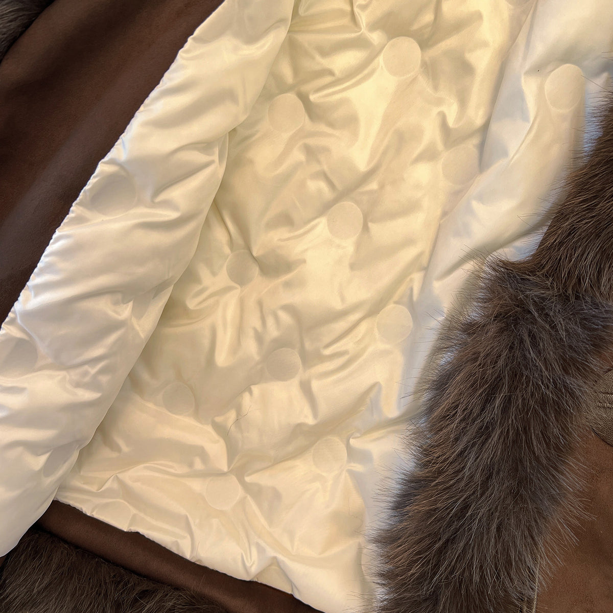 Cream quilted interior lining of a brown coat with dark plush trim