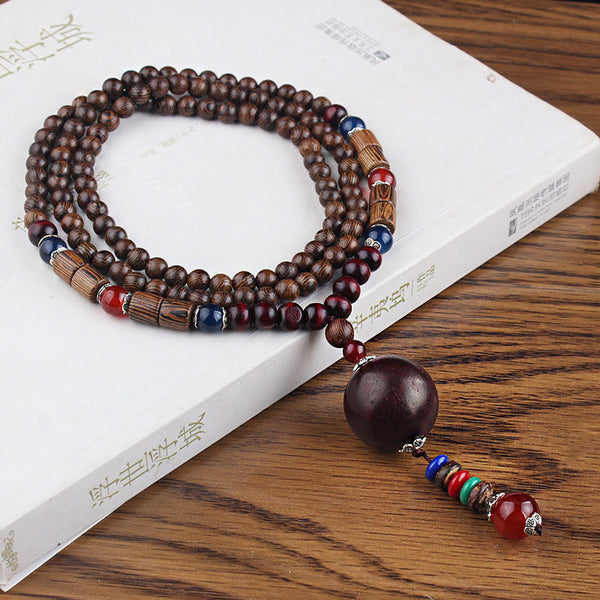 Brown beaded necklace with dark round pendant and multicolor hanging beads on a white book