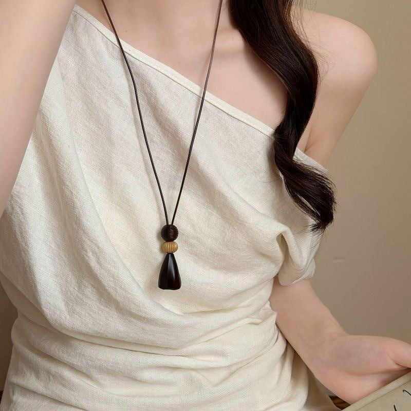 Dark tassel pendant necklace on a long cord, worn with a cream top