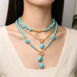 Model wearing layered turquoise-colored beads and gold-tone chains with drop pendants