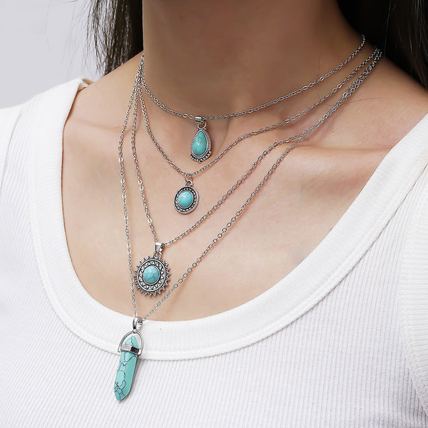 Layered silver-tone necklaces with turquoise-colored pendants, worn with a white top