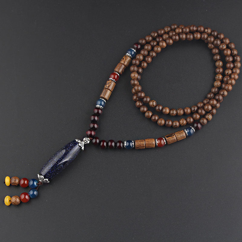 Long brown beaded necklace with dark elongated pendant on a charcoal background