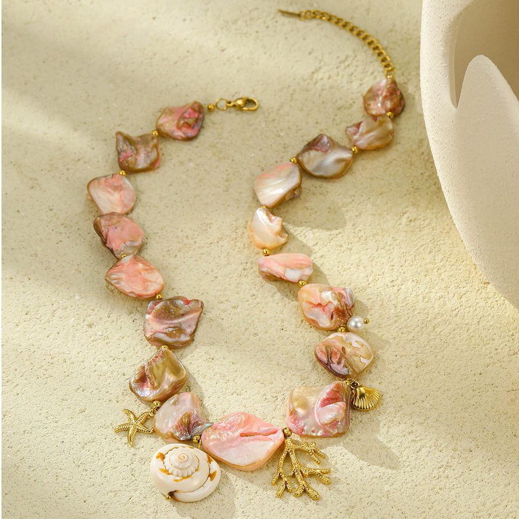 Pink shell-style necklace with gold-tone marine charms arranged on sand