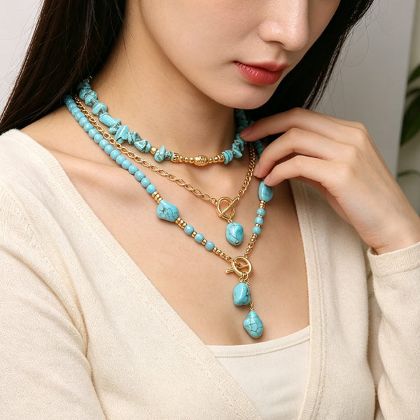 Turquoise-colored layered necklace with gold-tone chain and oval drop accents on a model